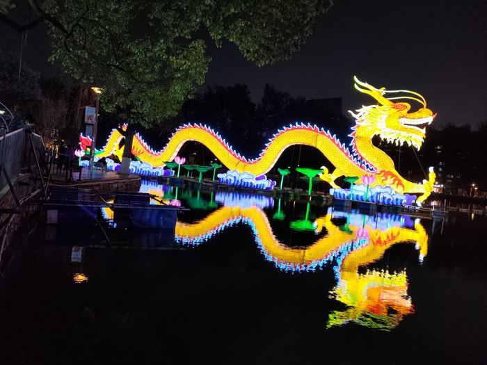 A long glowing yellow lantern dragon reflected in dark lake water at night