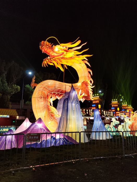 An orange glowing lantern dragon rising over colourful lantern hills at night
